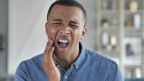 young man in blue shirt holding his jaw, signs of bruxism