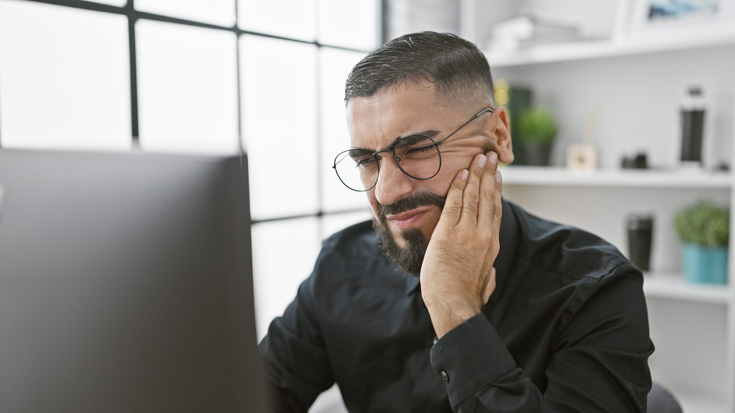young man working at computer with his hand on jaw, severe tooth ache