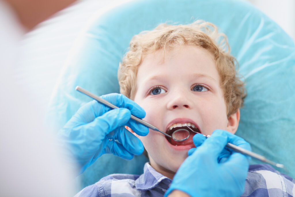 little boy having his teeth cleaned by a doctor in blue gloves