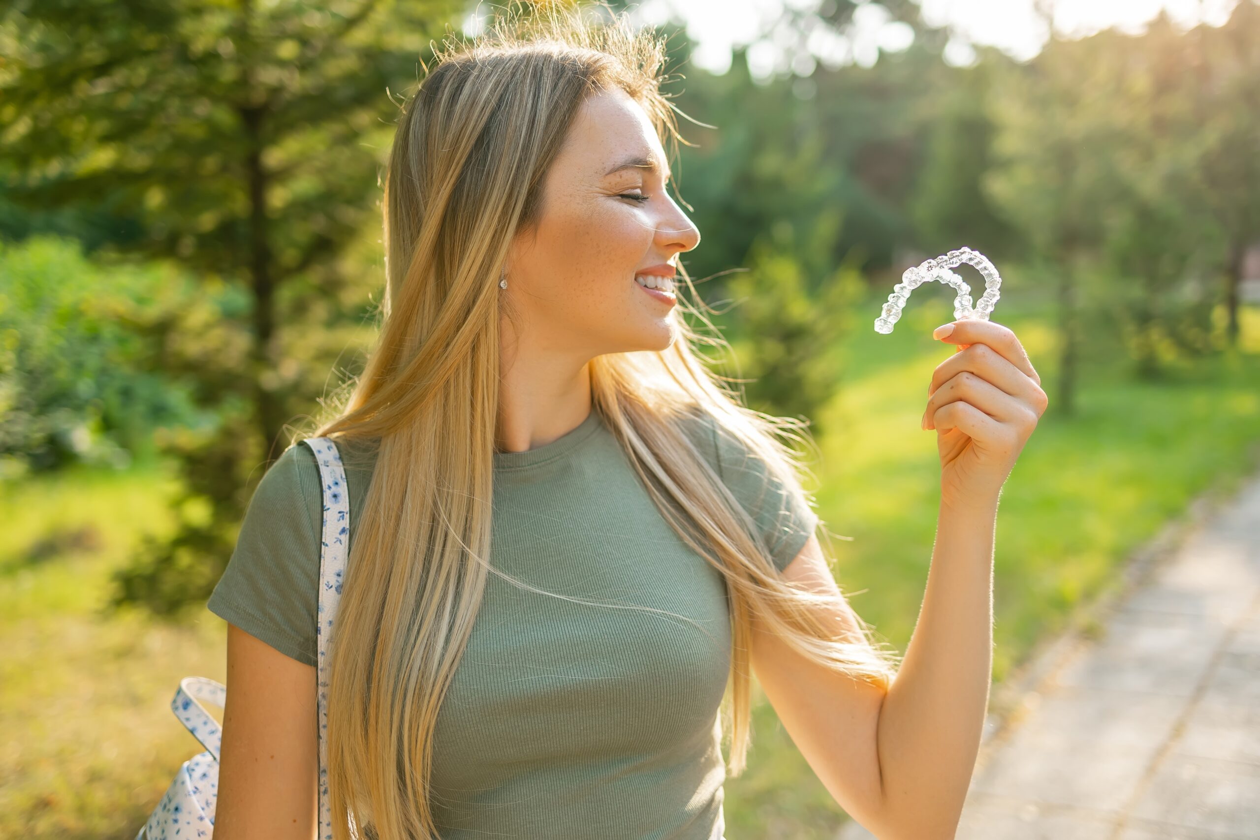 side view of a young woman outdoors, holding up clear aligners